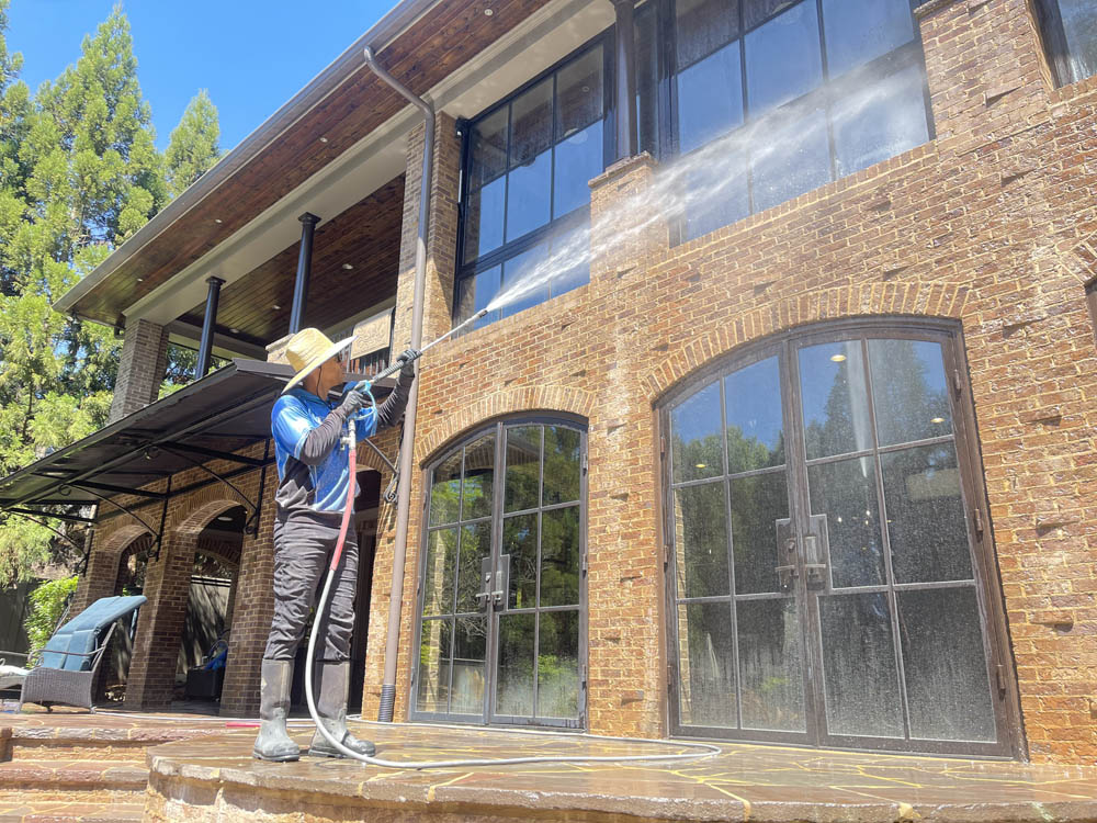 A Phenom technician soft-washing the brick facade and windows of a large Atlanta home